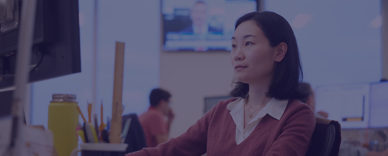 A woman looking at a desktop computer in an open office setting