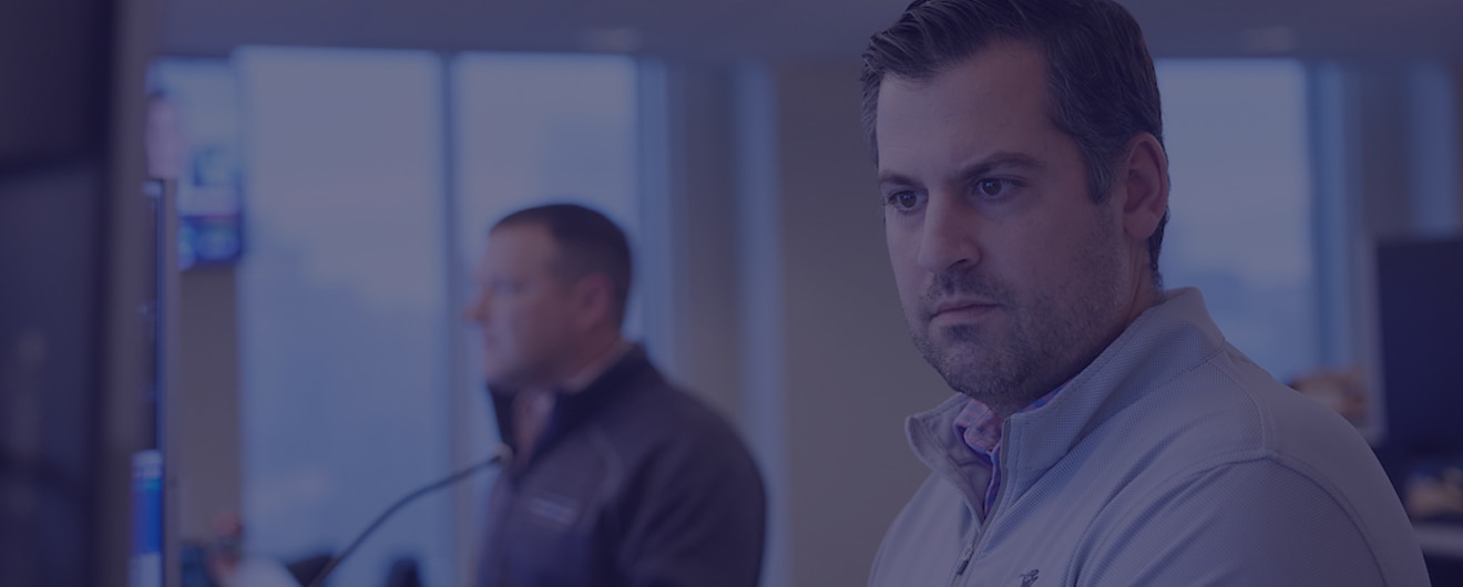 A man looking at a computer screen with his colleague in the background